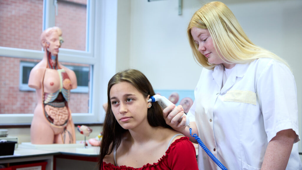 Photo of a student checking the temperature of another student with an ear thermometer