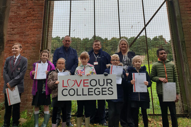 Local school children holding the "Love Our Colleges" sign in front of the gate.