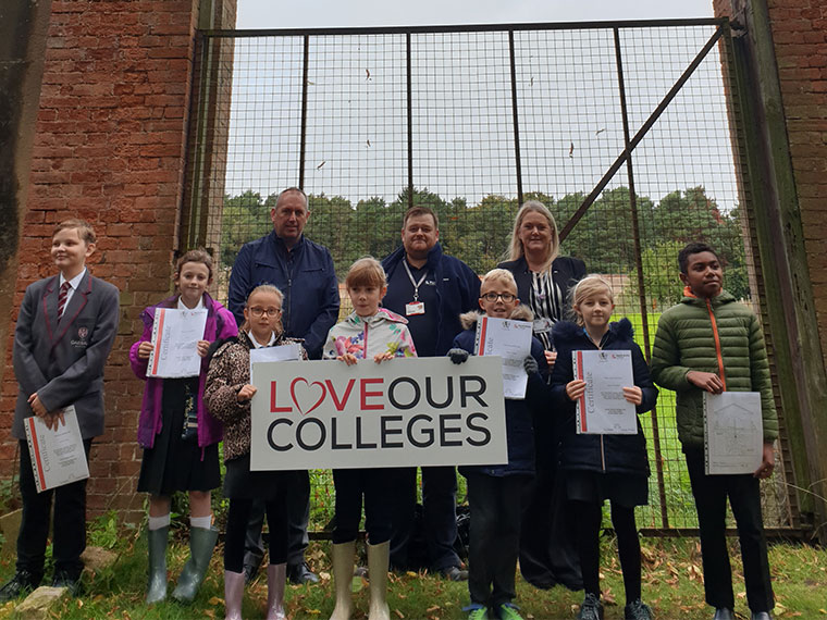 Local school children holding the "Love Our Colleges" sign in front of the gate.