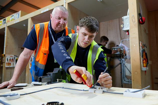 Electrical student cutting a rubber cable whilst being mentored by their tutor.